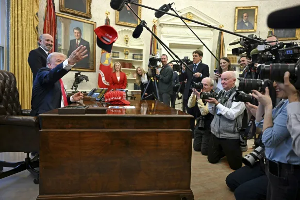 الرئيس الأميركي دونالد ترمب يجلس في المكتب البيضوي مع كومة من قبعات البيسبول الحمراء مكتوب عليها: «ترمب محق في كل شيء» (أ.ب)