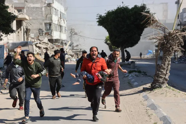 فلسطيني يحمل طفلة جريحة بعيدا عن موقع وسط قطاع غزة لجأ إليه نازحون واستهدفته ضربة إسرائيلية أمس (أ.ف.ب)