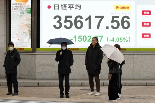 مشاة يسيرون تحت الأمطار أمام شاشة تعرض حركة الأسهم في العاصمة اليابانية طوكيو (إ ب أ)