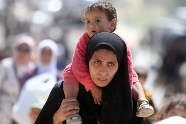 فلسطينية تحمل طفلاً يوم الاثنين وتفر من رفح جنوب غزة بعد أوامر إخلاء إسرائيلية (رويترز)