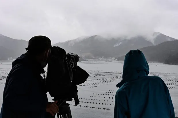 Members of the media look out across the bay at smoke rising from a mountain in the rain as firefighters continue to battle a wildfire near the city of Ofunato on March 5, 2025. (AFP)