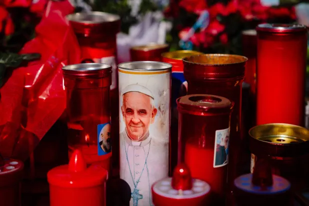 شموع عند تمثال البابا يوحنا بولس الثاني خارج مستشفى جيميلي الجامعي حيث يعالج البابا فرانسيس من الالتهاب الرئوي (أ.ف.ب)