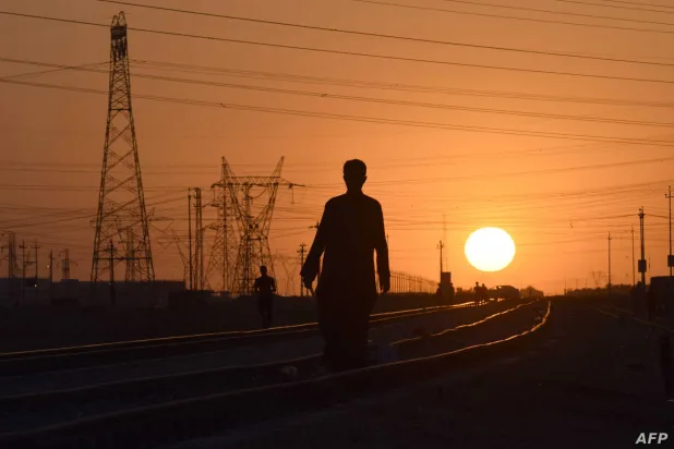 شخص يمر فوق خط سكة حديد وخلفه أبراج للضغط العالي وقت غروب الشمس (أ.ف.ب)