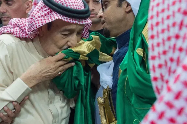 الملك سلمان مقبّلاً العلم السعودي (واس)