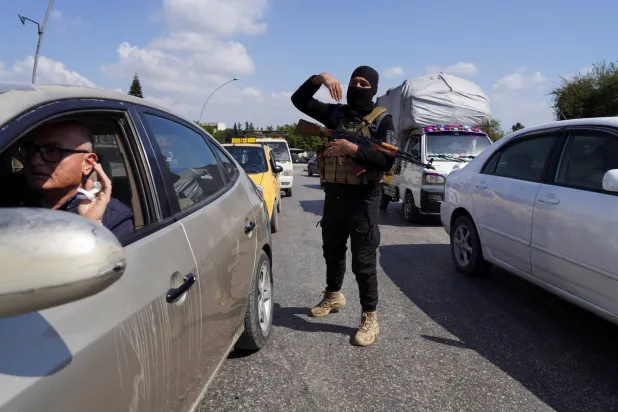 أحد أفراد قوات الأمن السورية يشير بيده وهو يقف بين السيارات في اللاذقية (رويترز)