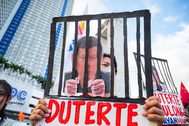 متظاهر يحمل لافتة تصوِّر الرئيس السابق رودريغو دوتيرتي خلف القضبان (د.ب.أ)