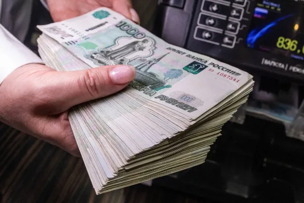 موظفة ببنك تحمل أوراقاً نقدية من فئة ألف روبل بجانب آلة لعدّ العملات في موسكو (رويترز)