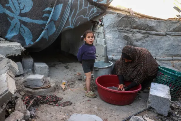 Gazze Şeridi'nin merkezindeki Bureyc kampında yanında bir çocukla bulaşık yıkayan Filistinli kadın (AFP)