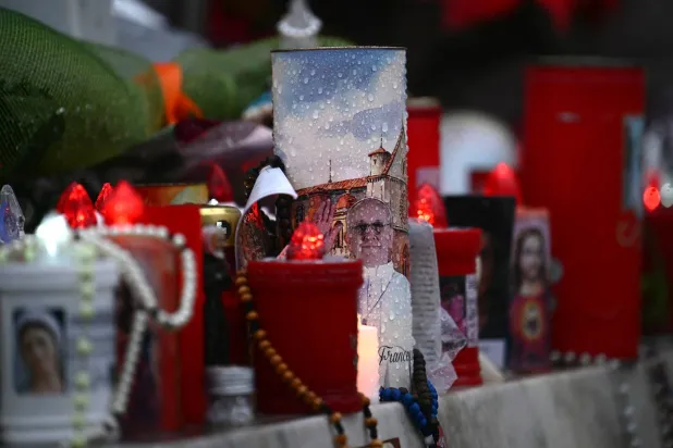 إضاءة شموع عند تمثال البابا يوحنا بولس الثاني خارج مستشفى جيميلي حيث يُعالج البابا فرنسيس بسبب الالتهاب الرئوي (أ.ف.ب)