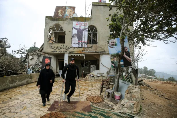 نعيمة قطيش ونجلها يسيران خارج منزلهما المتضرر جراء القصف الإسرائيلي على بلدة حولا بجنوب لبنان (د.ب.أ)