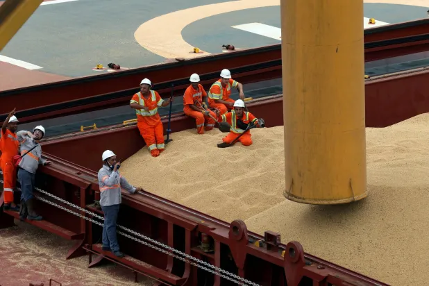 عمال على سفينة بضائع في ميناء سانتوس البرازيلي تحمل فول الصويا إلى الصين (رويترز)