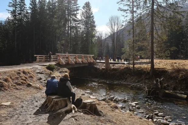 سياح يستريحون بالقرب من مجرى مائي أثناء سيرهم عبر وادي كوسيليسكا في جبال تاترا جنوب بولندا (إ.ب.أ)