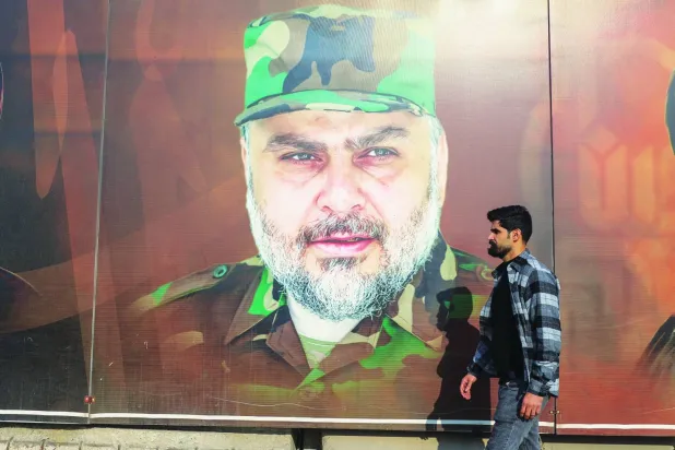 
  عراقي يمر أمام صورة لمقتدى الصدر (مرتدياً الزي العسكري الخاص بـ«سرايا السلام») في أحد شوارع بغداد (أ.ف.ب)