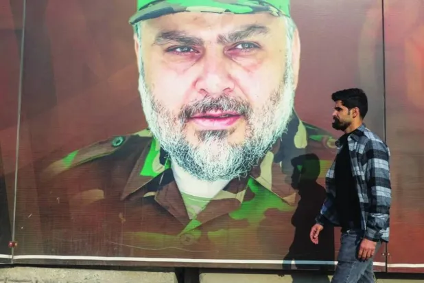 An Iraqi walks down a street in Baghdad, passing by a portrait of Moqtada al-Sadr wearing the military uniform of Saraya al-Salam (AFP)