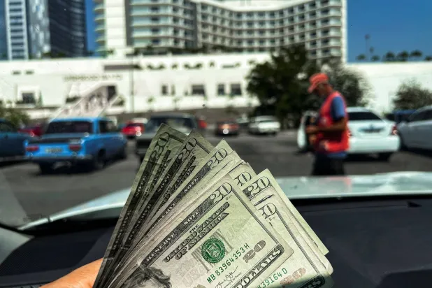 رجل يحمل أوراقاً نقدية بالدولار لالتقاط صورة أمام متجر يتعامل بالدولار فقط في هافانا (أ.ف.ب)
