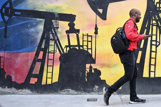رجل يسير أمام جدارية تُصوّر مضخة نفط في كاراكاس (أ.ف.ب)