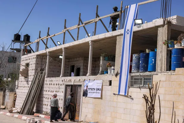 مستوطنون وجندي إسرائيلي بمدينة الخليل في الضفة الغربية يوم 24 مارس 2025 (أ.ف.ب)