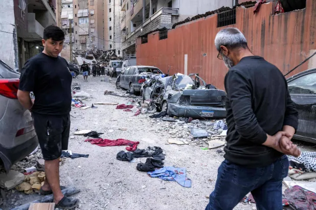 رجل يمشي بجوار مركبات متضررة في موقع غارة إسرائيلية على مبنى بالضاحية الجنوبية لبيروت (أ.ف.ب)