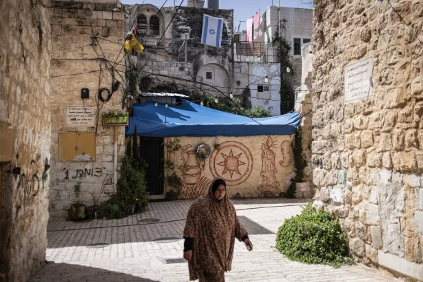 فلسطينية تمر قرب منزل رفع مستوطنون عليه العلم الإسرائيلي في وسط مدينة الخليل بالضفة الغربية الخميس (أ.ف.ب)