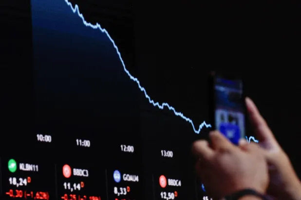 رجل يصور شاشة تعرض التقلبات التي تحدث في أسواق المال في ساوباولو بالبرازيل (رويترز)