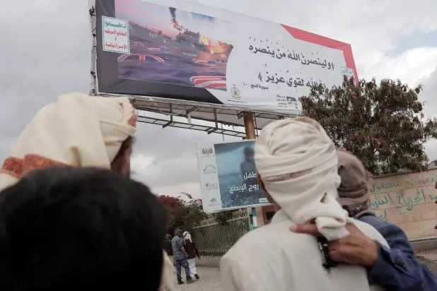 أتباع الحوثيين بجوار لوحة إعلانية تظهر صورة مفبركة لسفينة تحترق وهي ترفع العلم الأميركي (غيتي)