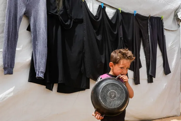 طفل فلسطيني يراقب أقرانه بينما ينتظرون الحصول على طعام من مطبخ خيري في خان يونس يوم الأحد (رويترز)