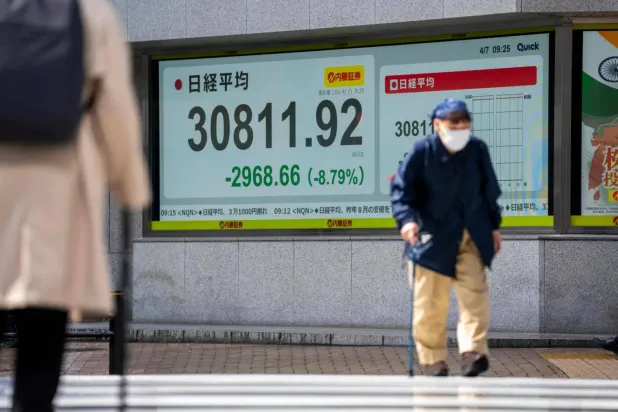 7 Nisan 2025 tarihinde Tokyo Menkul Kıymetler Borsası'nda Nikkei Endeksi rakamlarını gösteren elektronik bir panonun önünden geçen Japonlar
