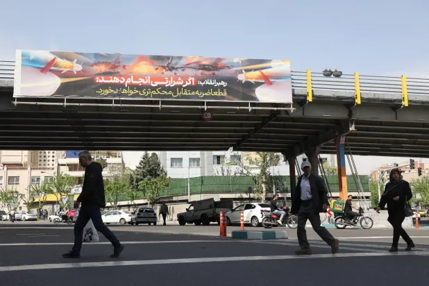 إيرانيون يسيرون إلى جانب لوحة إعلانية في أحد شوارع طهران تُحذر الولايات المتحدة من شن هجوم على إيران (رويترز)