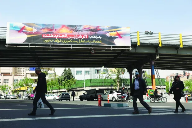 
إيرانيون يسيرون إلى جانب لوحة إعلانية في أحد شوارع طهران تُحذر الولايات المتحدة من شن هجوم على بلادهم (رويترز)