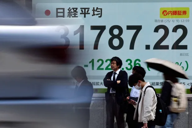 مارَّة يقفون أمام شاشة إلكترونية تعرض متوسط مؤشر «نيكي» الياباني (رويترز)