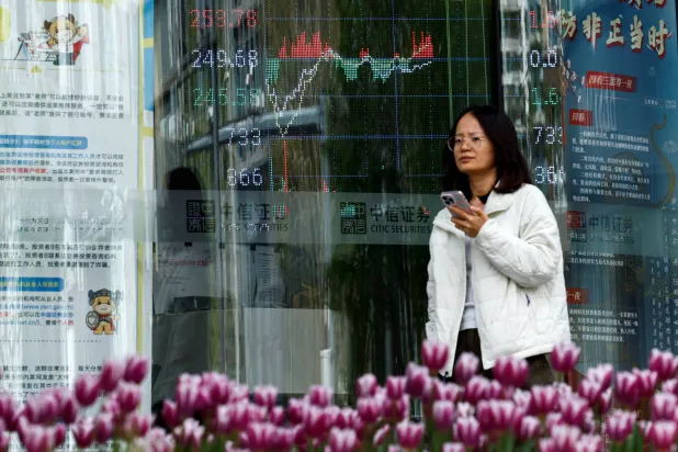 امرأة تمر أمام مكتب وساطة مالية يحمل لوحة تعرض معلومات مؤشر الأسهم في بكين (رويترز)