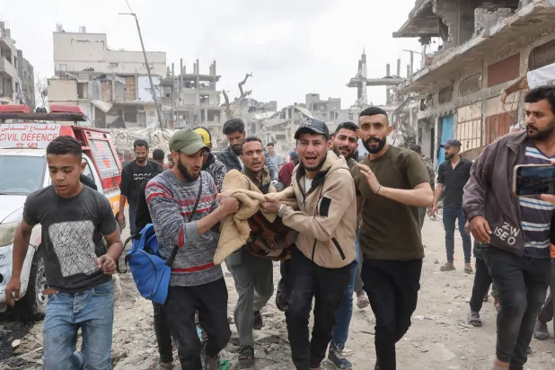 رجال يهرعون حاملين في بطانية أحد ضحايا الغارة الإسرائيلية على منطقة سكنية في حي الشجاعية (أ.ف.ب)
