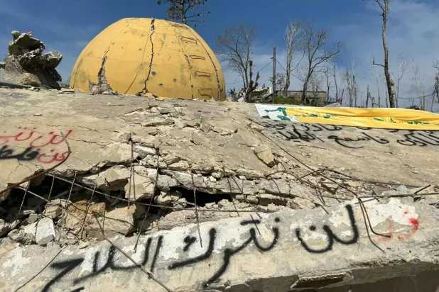 Lübnan'ın güneyindeki Ramiye kasabasında İsrail hava saldırılarında yıkılan bir caminin enkazı üzerine Hizbullah destekçileri tarafından yazılan “Silah bırakmayacağız” sloganı (AFP)