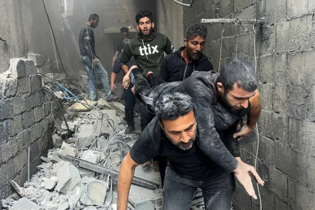 Filistinliler, dün Gazze Şehri'ndeki Şucaiye mahallesini hedef alan İsrail hava saldırısının ardından yaralı bir adamı taşıyor (Reuters)