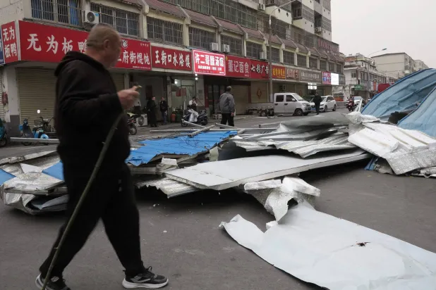 رجل يسير في شارع ملأه حطام سببته الرياح في مدينة فويانغ الصينية (أ.ف.ب)