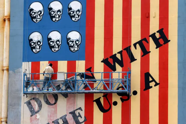 یک نقاش ایرانی در حال بازسازی و رنگ‌آمیزی دوباره یک نقاشی دیواری ضد آمریکایی در تهران است (خبرگزاری فرانسه)