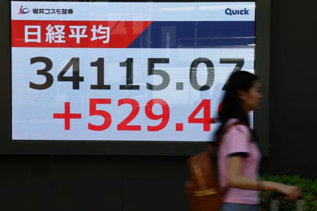 امرأة تمر أمام لوحة أسعار أسهم تعرض متوسط ​​أسهم نيكي خارج مكتب وساطة في طوكيو (رويترز)