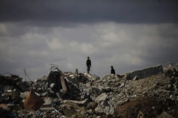 فلسطينيون نازحون يسيرون يوم الاثنين على أنقاض المباني المنهارة في مخيم البريج وسط غزة (د.ب.أ)