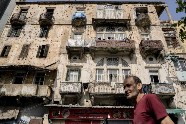 رجل يسير أمام مبنى ممتلئ بثقوب الرصاص في بيروت (أ.ب)