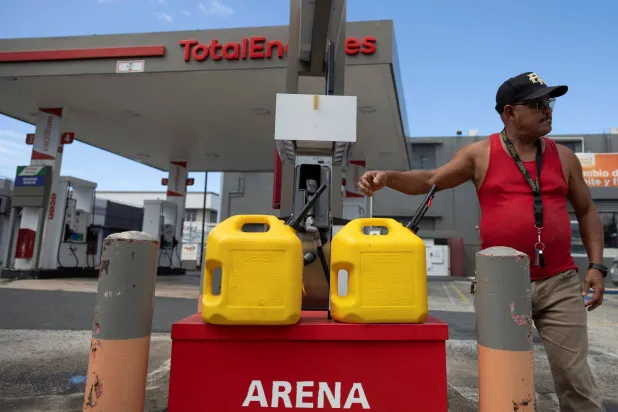 رجل يقف بجوار حاويات تحتوي على وقود ديزل بعد انقطاع التيار الكهربائي الشامل في بورتوريكو (رويترز)