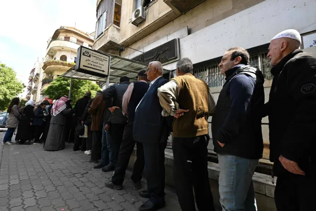 أشخاص ينتظرون دورهم في طابور خارج ماكينة صراف آلي في دمشق (أ.ف.ب)