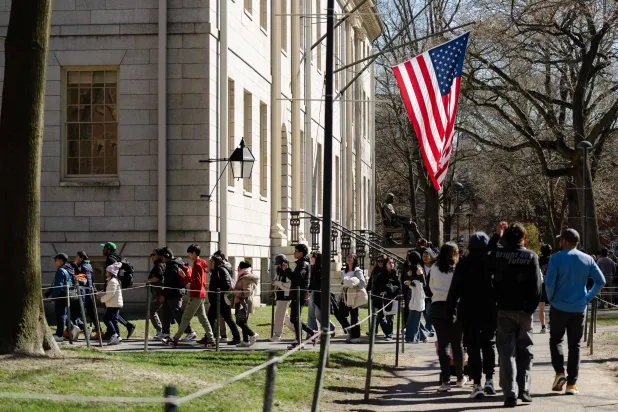 سياح يمرون بجوار العلم الأميركي الذي يرفرف في جامعة هارفارد (أ.ف.ب)