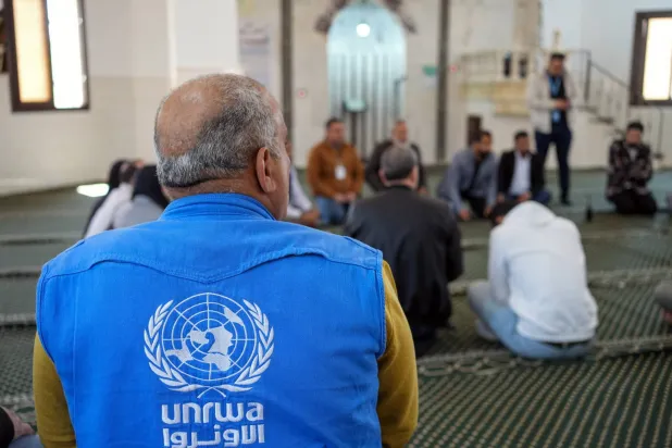 رجل يرتدي سترة يظهر عليها شعار وكالة الأمم المتحدة لغوث وتشغيل اللاجئين الفلسطينيين (الأونروا) (إ.ب.أ)