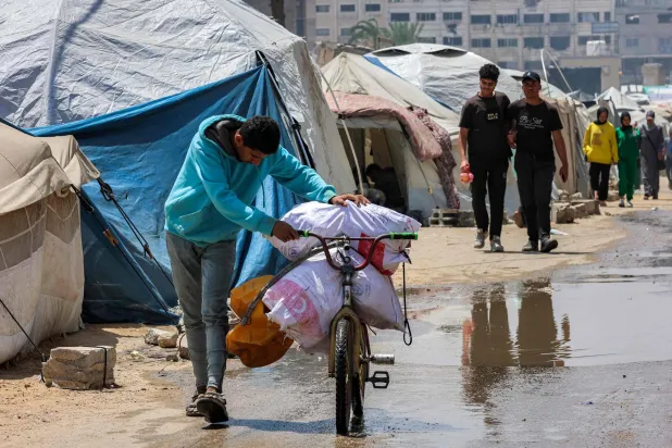 صبي يدفع دراجة محمَّلة بأكياس مساعدات غذائية أمام خيام في مدينة غزة (أ.ف.ب)