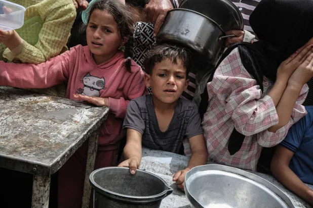 أطفال فلسطينيون ينتظرون توزيع الطعام يوم الثلاثاء في مخيم النصيرات للاجئين وسط غزة (د.ب.أ)