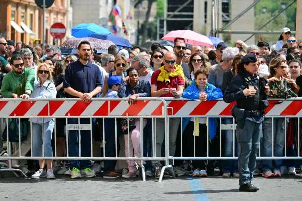 الزوار يقفون بجانب الحواجز وبجانب ضابط شرطة إيطالي في انتظار دخول كاتدرائية القديس بطرس وتقديم واجب العزاء للبابا الراحل (أ.ف.ب)