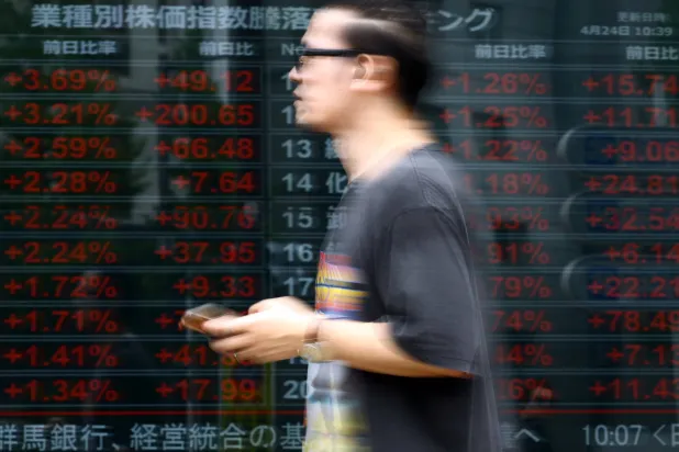 رجل يمرّ بجانب شاشة إلكترونية تعرض مؤشرات أسعار الأسهم القطاعية في طوكيو (رويترز)