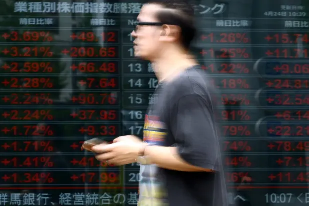 Tokyo'da sektörel hisse senedi fiyat endekslerini gösteren elektronik ekranın önünden geçen bir adam (Reuters)