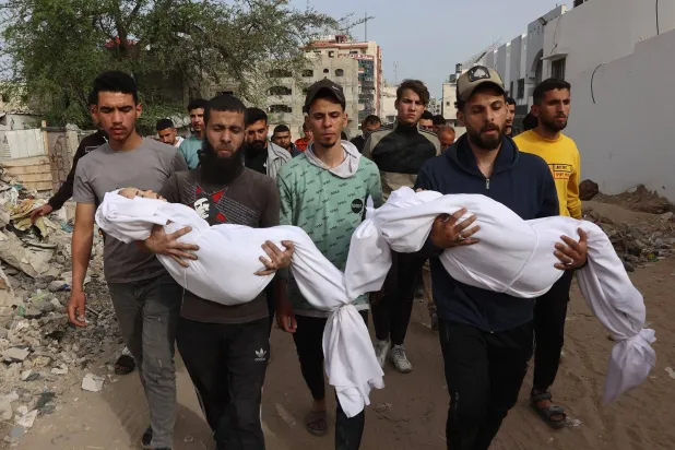 فلسطينيون يحملون جثث أقاربهم المُكفنة الذين قُتلوا في غارة إسرائيلية على مدرسة بغزة خلال وقت سابق (أ.ف.ب)