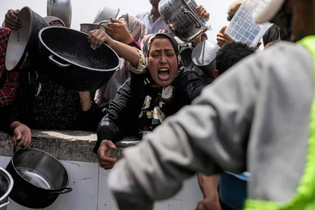 يصطف الناس حاملين أواني الطعام لتلقي وجبات خيرية من مطبخ في بيت لاهيا شمال قطاع غزة (أ.ف.ب)